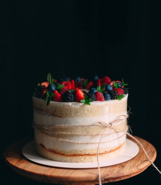 Meyveli kek. Kek, siyah arka plandaki ahşap bir stantta böğürtlenlerle süslenmiş..