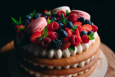 Meyveli kek. Kek, siyah arka plandaki ahşap bir stantta böğürtlenlerle süslenmiş..