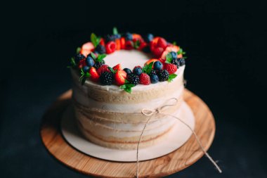 Meyveli kek. Kek, siyah arka plandaki ahşap bir stantta böğürtlenlerle süslenmiş..