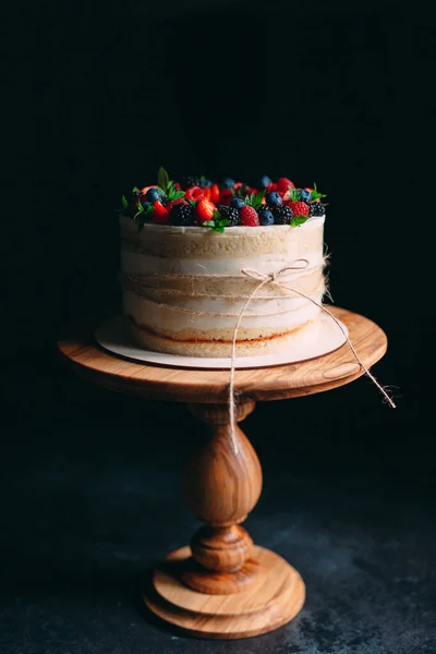 Ovocný dort. Dort zdobený bobulemi na dřevěném stojanu na černém pozadí. — Stock fotografie