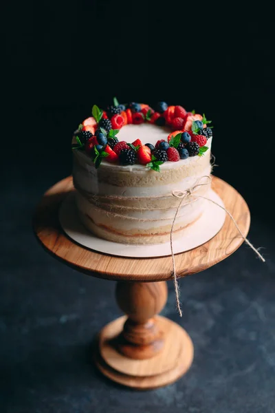 Kue buah. Kue dihiasi dengan buah beri di stand kayu dengan latar belakang hitam. — Stok Foto