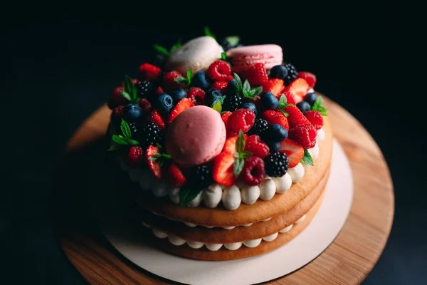 Pastel de frutas. Pastel decorado con bayas en un soporte de madera sobre un fondo negro. — Foto de Stock