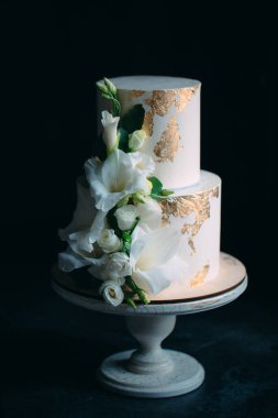 Siyah arka planda, ahşap bir stantta çiçekli iki katlı bir pasta..