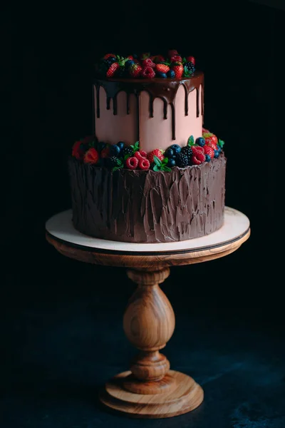 Ovocný čokoládový dort na dřevěném stojanu na černém pozadí. — Stock fotografie