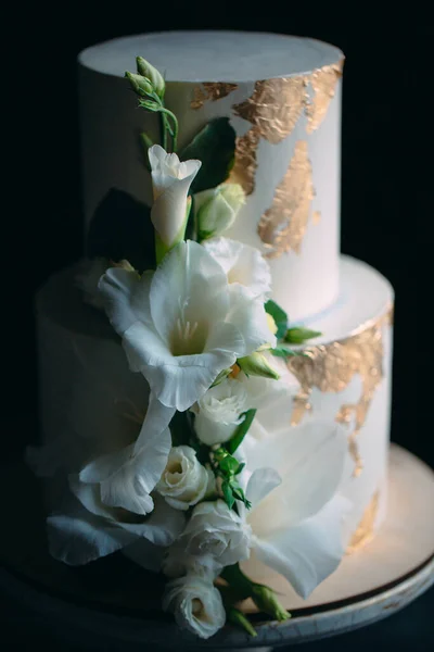 Torta a due livelli con fiori su un supporto di legno su uno sfondo nero. — Foto Stock