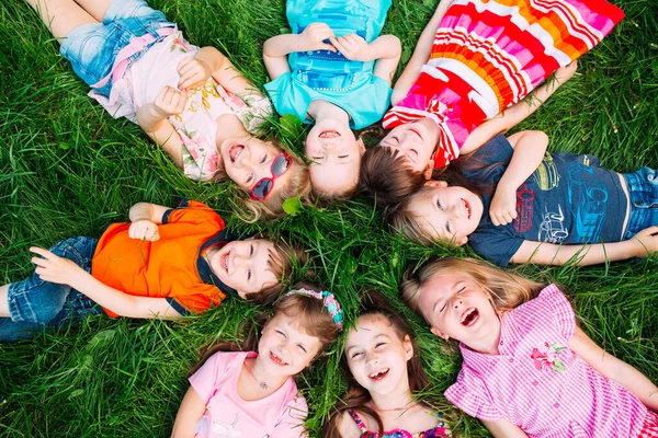 Un grupo de niños tumbados en la hierba verde del parque. La interacción de los niños. —  Fotos de Stock