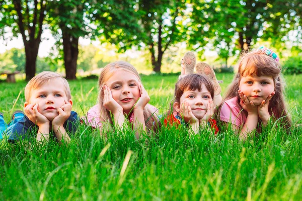 Eine Gruppe Kinder liegt auf dem grünen Rasen im Park. Die Interaktion der Kinder. — Stockfoto
