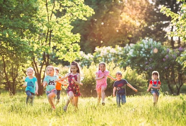 Duża grupa dzieci, przyjaciół chłopców i dziewcząt biegających w parku w słoneczny letni dzień w luźnych ubraniach . — Zdjęcie stockowe