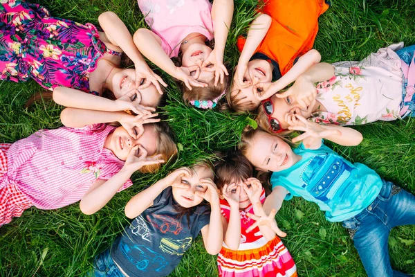 Eine Gruppe Kinder liegt auf dem grünen Rasen im Park. Die Interaktion der Kinder. — Stockfoto