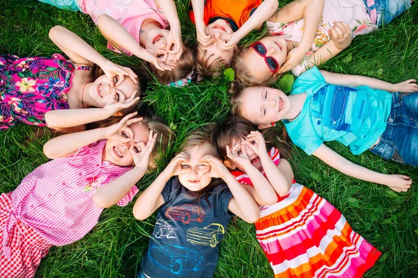 Eine Gruppe Kinder liegt auf dem grünen Rasen im Park. Die Interaktion der Kinder. — Stockfoto