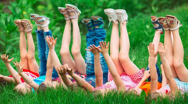 Діти лежать на зеленій траві в парку в літній день з піднятими ногами в небо . — стокове фото