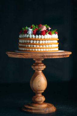 Meyveli kek. Kek, siyah arka plandaki ahşap bir stantta böğürtlenlerle süslenmiş..