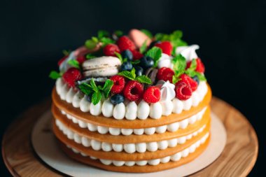 Meyveli kek. Kek, siyah arka plandaki ahşap bir stantta böğürtlenlerle süslenmiş..