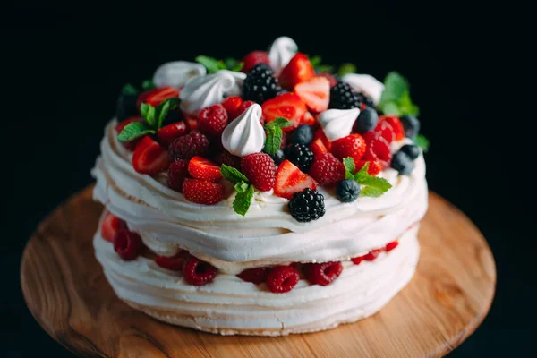 Fruit cake. Cake decorated with berries on a wooden stand on a black background. — Stock Photo, Image