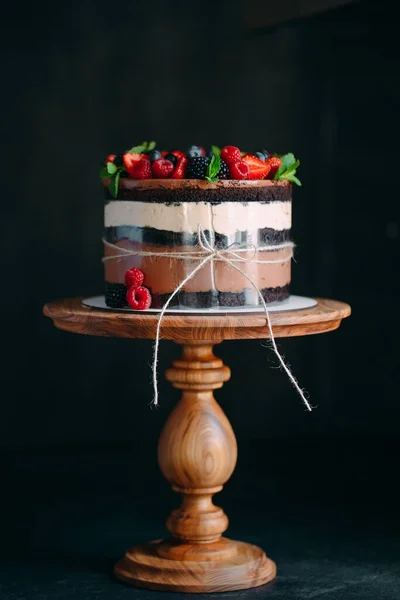 Fruit cake. Cake decorated with berries on a wooden stand on a black background. — Stock Photo, Image