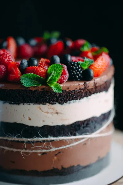 Fruitcake. Taart versierd met bessen op een houten statief op een zwarte achtergrond. — Stockfoto