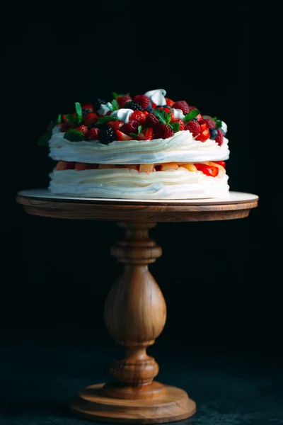 Fruit cake. Cake decorated with berries on a wooden stand on a black background. — Stock Photo, Image