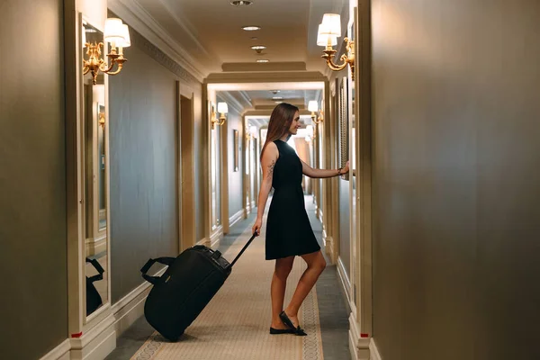 Молодая женщина с сумочкой и чемоданом в элегантном костюме идет по коридору гостиницы к себе в номер. — стоковое фото