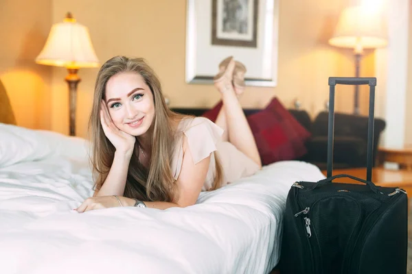 Le ung affärskvinna i sängen och stirra på kameran. Hotellrum. flickan slickar på sängen nära resväskan. — Stockfoto