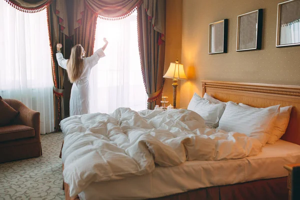 Mujer en albornoz estancia cerca de la ventana en la habitación del hotel. —  Fotos de Stock