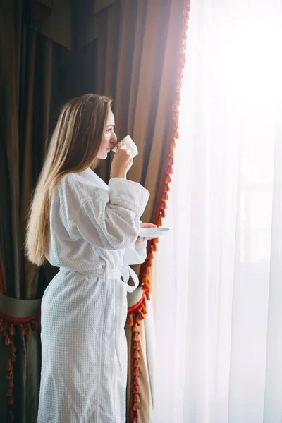 Девочка сидит у окна и пьет утренний кофе в гостиничном номере или дома. — стоковое фото