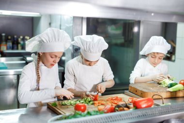 Çocuklar bir restoranın mutfağında sebze öğütür..