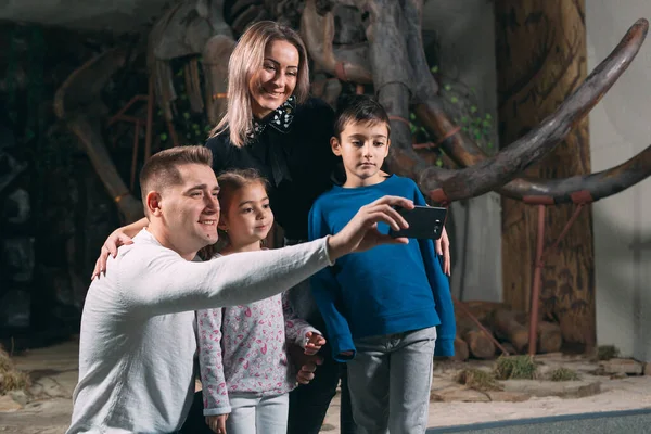 A family takes a selfie against a mammoth skeleton at the Museum of paleontology. — Stock Photo, Image