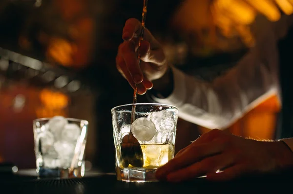 Bartendern rör om en sked whisky med is i ett glas. — Stockfoto