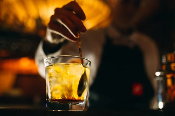 Bartendern rör om en sked whisky med is i ett glas. — Stockfoto