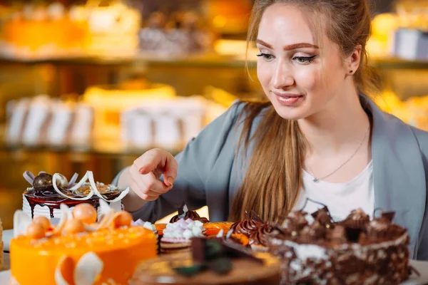 Girl looking at the bakery window with different pieces of cakes.