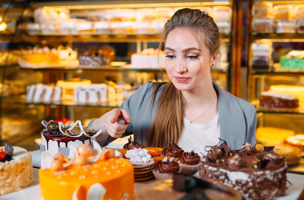 Girl looking at the bakery window with different pieces of cakes.