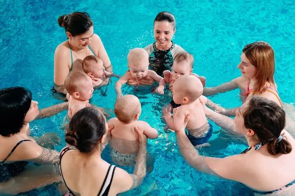 Een groep moeders met hun jonge kinderen in een zwemklas met een coach. — Stockfoto