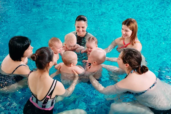 Eine Gruppe Mütter mit ihren kleinen Kindern im Kinderschwimmkurs mit einem Trainer. — Stockfoto