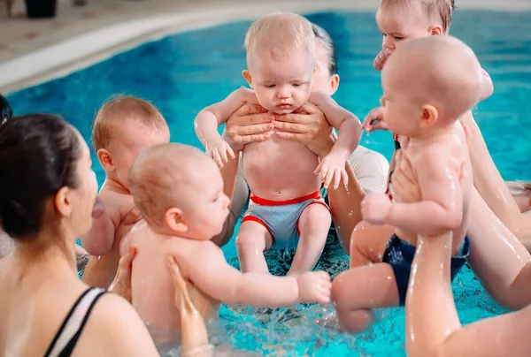 Un groupe de mères avec leurs jeunes enfants dans une classe de natation pour enfants avec un entraîneur. — Photo