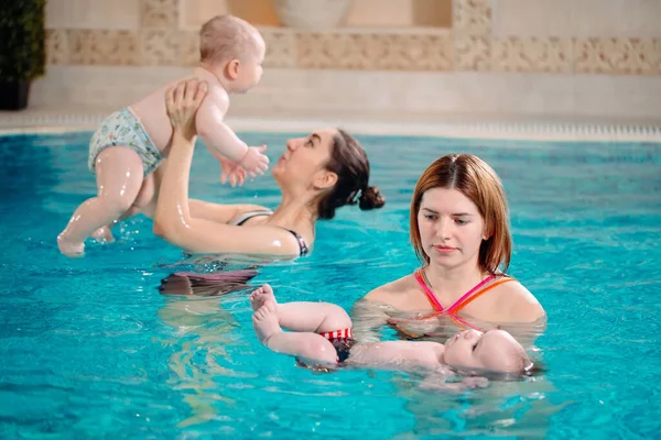 Eine Gruppe Mütter mit ihren kleinen Kindern im Kinderschwimmkurs mit einem Trainer. — Stockfoto