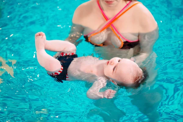 Eine Gruppe Mütter mit ihren kleinen Kindern im Kinderschwimmkurs mit einem Trainer. — Stockfoto