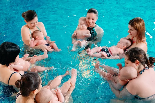 Eine Gruppe Mütter mit ihren kleinen Kindern im Kinderschwimmkurs mit einem Trainer. — Stockfoto