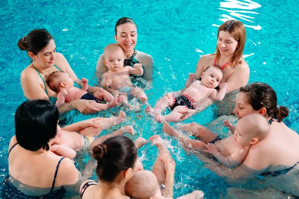 Eine Gruppe Mütter mit ihren kleinen Kindern im Kinderschwimmkurs mit einem Trainer. — Stockfoto