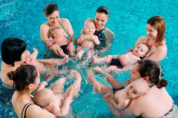 Un groupe de mères avec leurs jeunes enfants dans une classe de natation pour enfants avec un entraîneur. — Photo