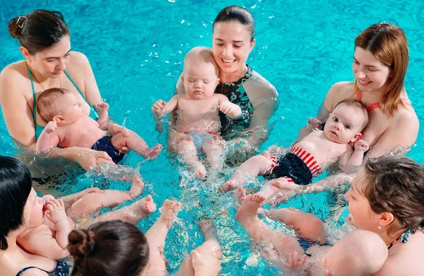 Een groep moeders met hun jonge kinderen in een zwemklas met een coach. — Stockfoto