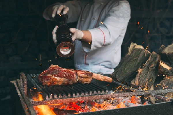 Chef pimenta o bife em uma fogueira. — Fotografia de Stock