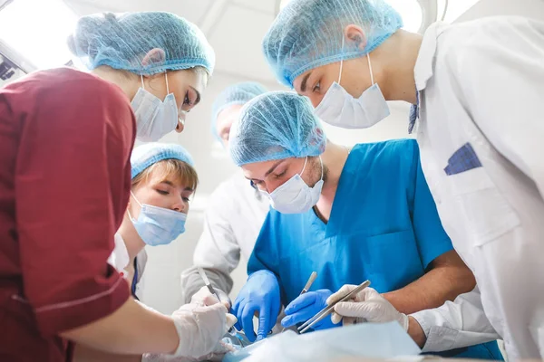 Grupo de cirujanos trabajando en quirófano. Equipo de medicina de reanimación con máscaras protectoras que sostienen herramientas médicas de acero —  Fotos de Stock