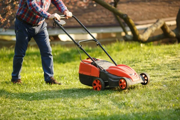 Maaimachine - werknemer maait gras in groene tuin bij zonsondergang. Man met elektrische grasmaaier, grasmaaier. Tuinier trimmen een tuin. — Stockfoto