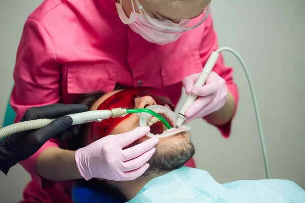 Professionell tandrengöring. Tandläkare rengör tänderna på en manlig patient. — Stockfoto