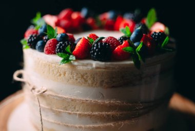 Meyveli kek. Kek, siyah arka plandaki ahşap bir stantta böğürtlenlerle süslenmiş..