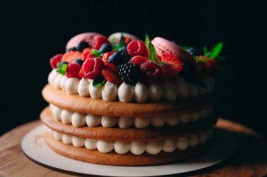 Meyveli kek. Kek, siyah arka plandaki ahşap bir stantta böğürtlenlerle süslenmiş..