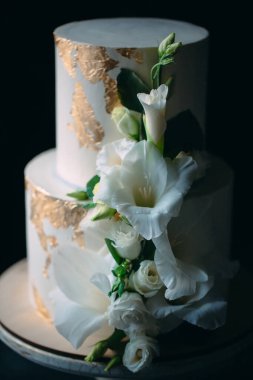 Siyah arka planda, ahşap bir stantta çiçekli iki katlı bir pasta..