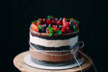 Meyveli kek. Kek, siyah arka plandaki ahşap bir stantta böğürtlenlerle süslenmiş..