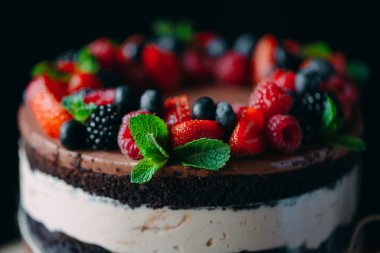 Meyveli kek. Kek, siyah arka plandaki ahşap bir stantta böğürtlenlerle süslenmiş..