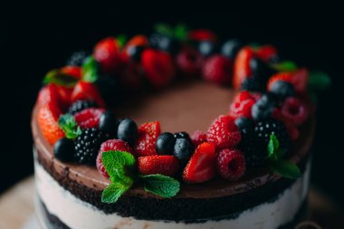 Meyveli kek. Kek, siyah arka plandaki ahşap bir stantta böğürtlenlerle süslenmiş..